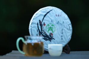 Close-up of packaged Puerh tea with glass teapot and cup outdoors during the day.